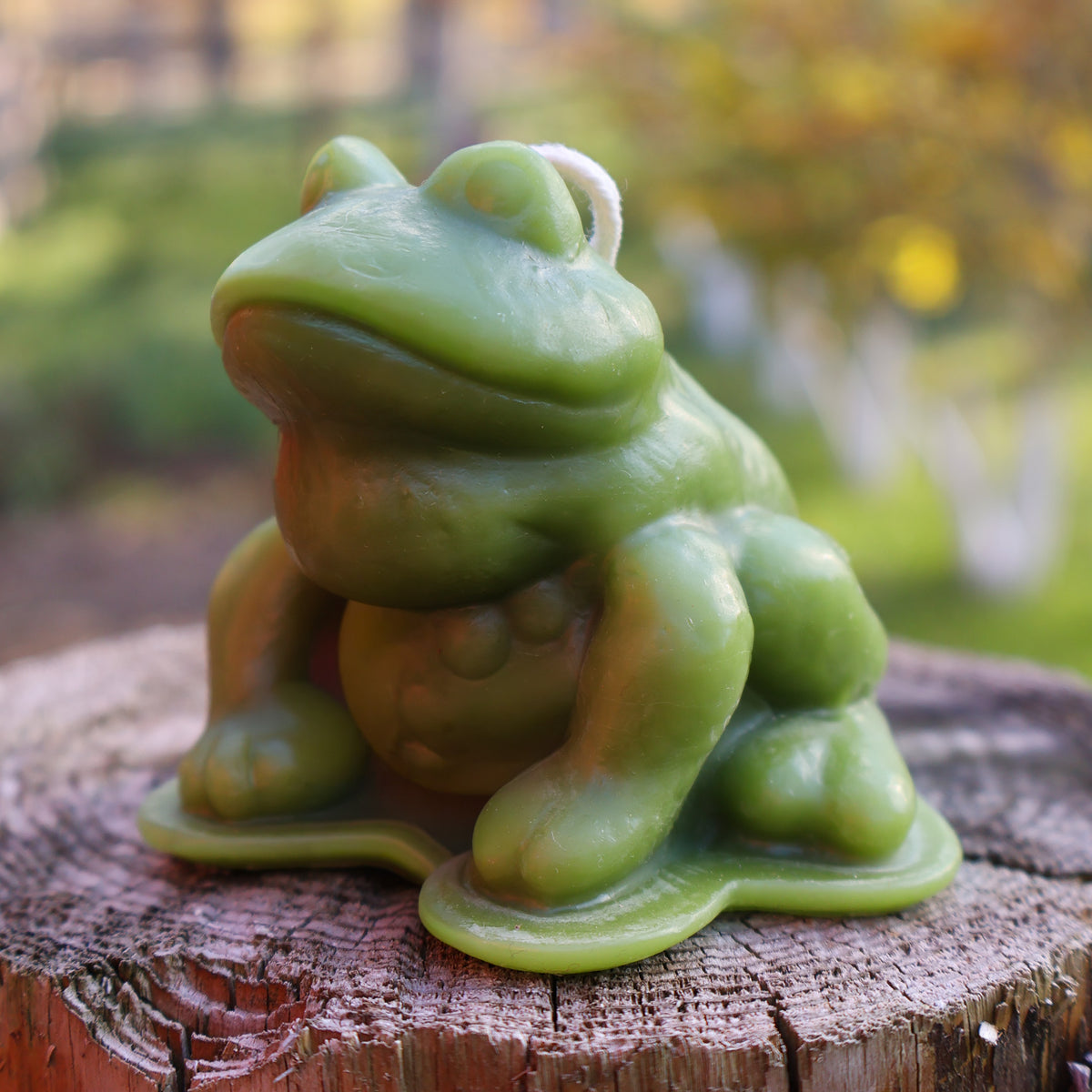 Green frog sculpture on a wooden stump with a blurred natural background