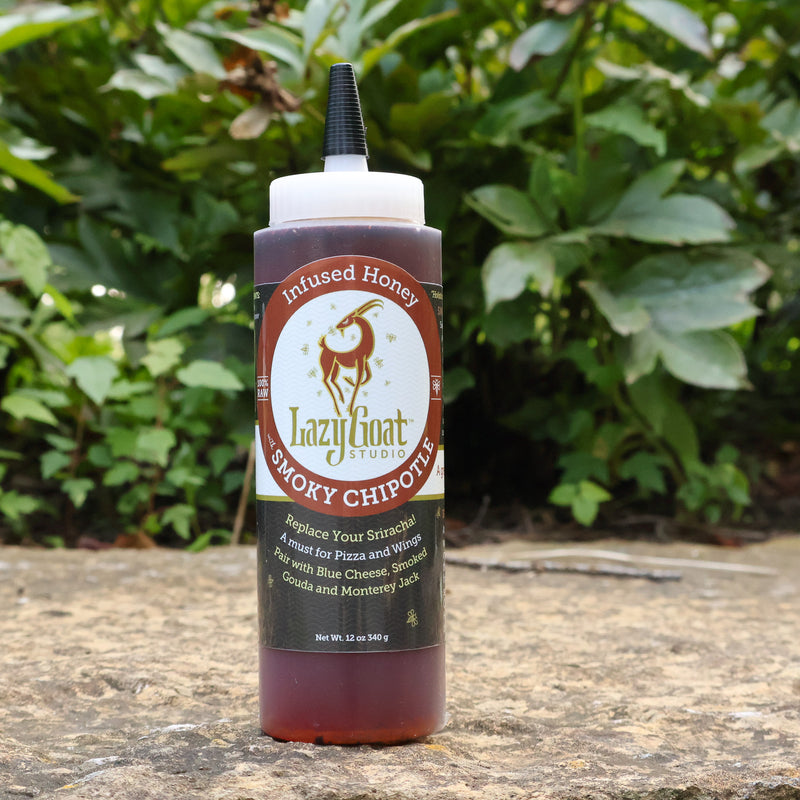 Bottle of Lazy Goat Studio Smoky Chipotle Infused Honey on a stone surface with greenery in the background